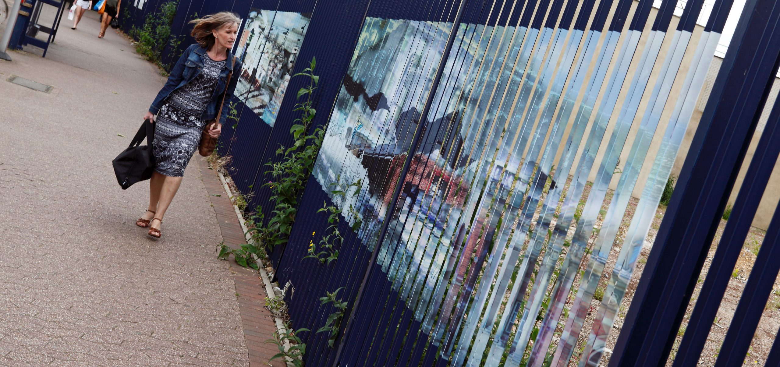 Female walking past artwork installed on fencing