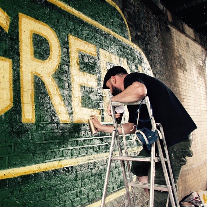 artist spray painting mural art work under station bridge