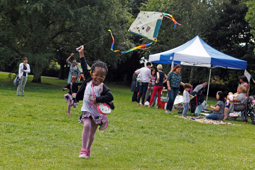young girl running in park flying a handmade kite