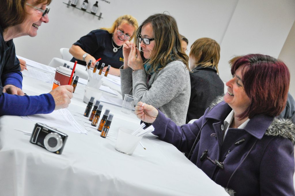 three woman sat at table, testing essences